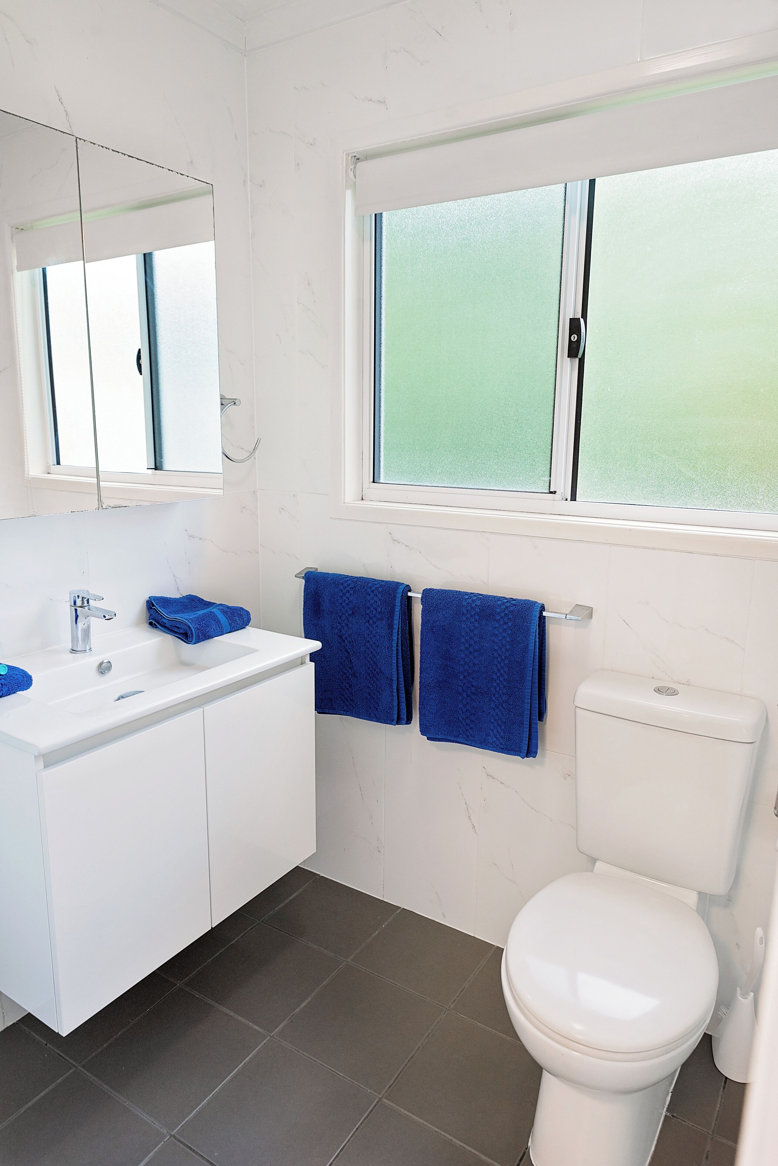 A bathroom with a white sink, mirror, and toilet, and a window with frosted glass.