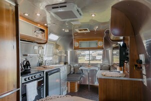 Interior compacto de una caravana con kitchenette, zona de estar y ventana con vistas al exterior.