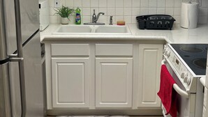 Une cuisine avec des meubles blancs, un réfrigérateur en acier inoxydable, un évier, une cuisinière et un plancher en bois.