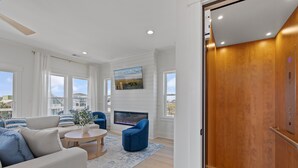 Una sala de estar moderna con sofá, sillón, mesa de centro, chimenea y ventanas amplias.