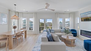 Amplia sala de estar con mesa de comedor, sofás, chimenea y ventanas grandes que ofrecen vistas al exterior.