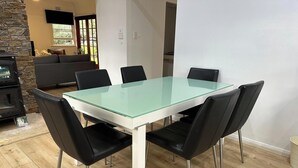 A dining area with a glass-top table, black chairs, a stone wall, and a fireplace. - KozyGuru | Wyong | Cottage Close to Everything (Wyong)
