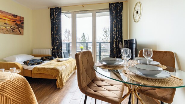 Une chambre d’hôtel moderne, équipée d’un lit, d’une table à manger avec des chaises, d’un balcon avec des rideaux et d’un tableau au mur.