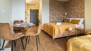 Une chambre d’hôtel comprenant un lit, une table de chevet avec une lampe, une table à manger avec des chaises et une porte donnant sur une autre pièce.