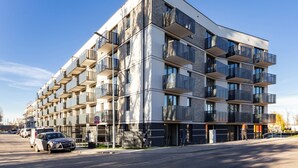 Un immeuble moderne à plusieurs étages, doté de balcons, d’un espace de stationnement et d’une enseigne indiquant la présence d’un hôpital.