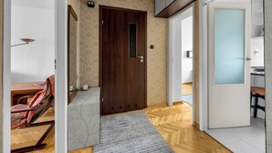A hallway with a wooden door, a patterned wall, a herringbone floor, and a white door with frosted glass. - Afrykańska Standard Apartment (Warszawa)