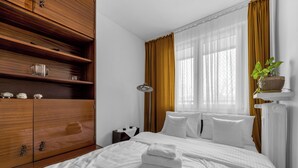A hotel room with a large bed, a wooden wardrobe, a bedside table, a lamp, and a window with curtains. - Afrykańska Standard Apartment (Warszawa)
