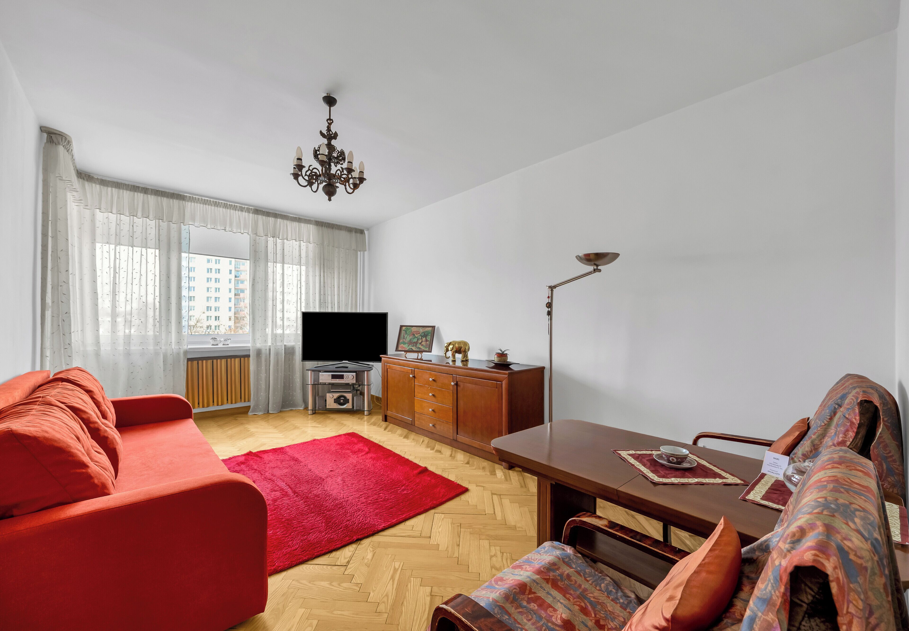 A living room with a red sofa, a dining table, a TV, and a radiator.