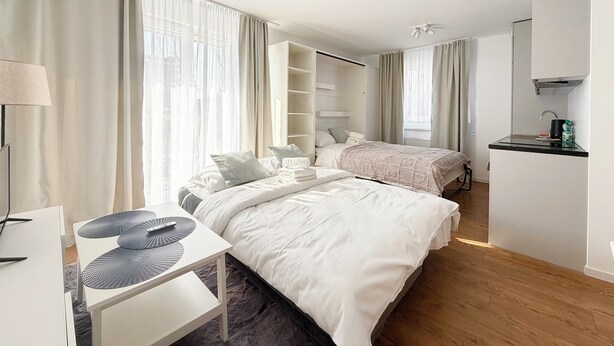 Habitació d'hotel moderna amb dos llits, una escriptori, un armari i una cuineta.