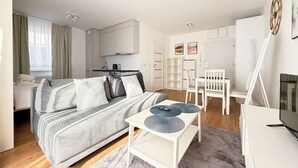 Habitació moderna i ben il·luminada amb llit, taula petita, televisió i cuineta.