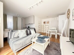 A modern, well-lit room with a bed, a small table, a TV, and a kitchenette. - Mieszczańska Charming Studio (Wrocław)