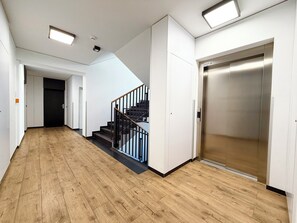 A hallway with wooden flooring, a staircase with black railings, and a modern elevator. - Mieszczańska Charming Studio (Wrocław)