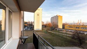 Een balkon met uitzicht op een parkeerplaats, een hoog gebouw met het nummer 82, en een geel gebouw in de verte.