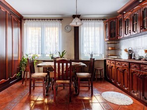 A traditional kitchen with wooden cabinets, a dining table with chairs, and a window with sheer curtains. - Podgórska Comfort Apartment (Gdynia)