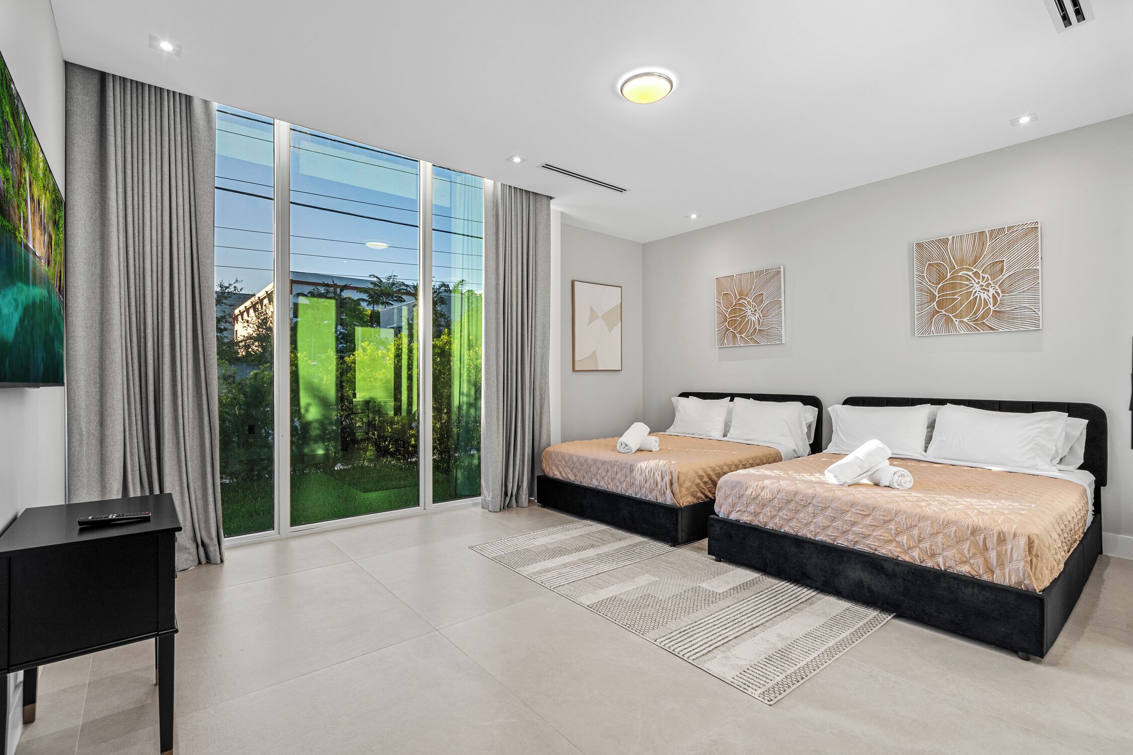 A modern hotel room with two beds, a large sliding glass door to a garden, and a black nightstand.
