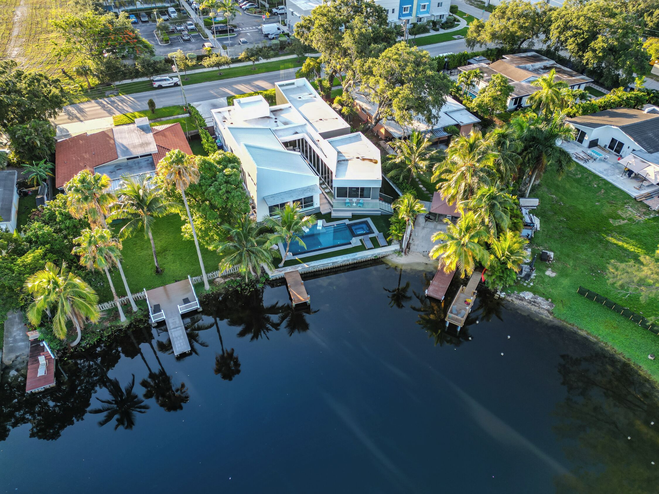 An aerial view of a residential area with a swimming pool, palm trees, and modern houses.
