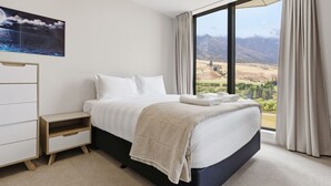 A bedroom with a bed, a nightstand, a dresser, and a large window with a mountain view. - Mountain Ash View - Remarkable Apartment (Queenstown)