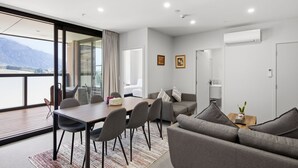 A modern living room with a dining area, a sofa, a coffee table, and a view of mountains. - Mountain Ash View - Remarkable Apartment (Queenstown)