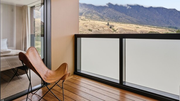 A balcony with a view of mountains, a wooden floor, and a leather chair. - Mountain Ash View - Remarkable Apartment (Queenstown)