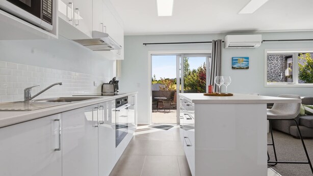Une cuisine moderne avec des meubles blancs, un îlot central et une vue sur une terrasse extérieure.