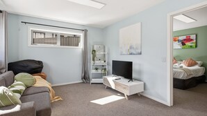 Une chambre moderne avec un lit, un téléviseur posé sur un meuble, une fenêtre et une porte donnant sur une autre pièce.