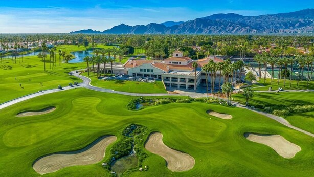 Ein Golfplatz mit Clubhaus, Palmen und Bergen im Hintergrund.