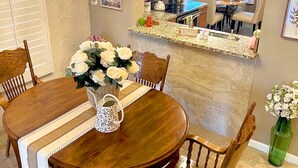 Ein Essbereich mit einem Holztisch, Stühlen, einer Chandelüster und einer Blumenvase.