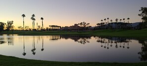 A golf course with a pond reflecting palm trees and a building in the background.