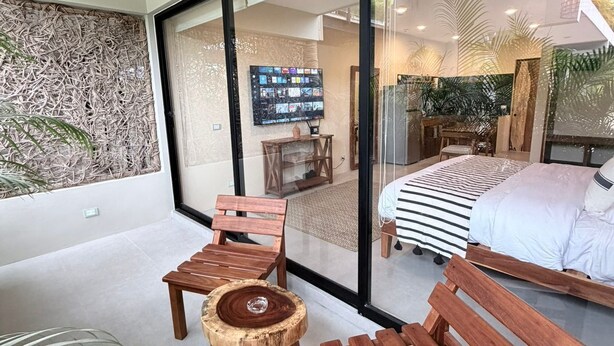 Um interior moderno com uma grande porta de vidro deslizante que dá para um quarto, um banco de madeira e uma pequena mesa redonda.