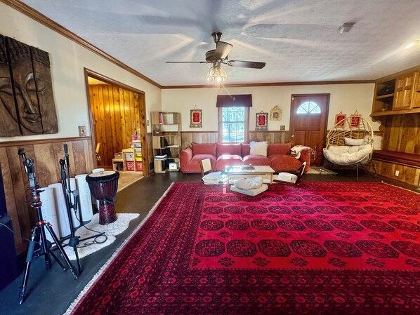 Una habitación con alfombra roja, un ventilador de techo, una estantería de madera y una ventana con vistas.
