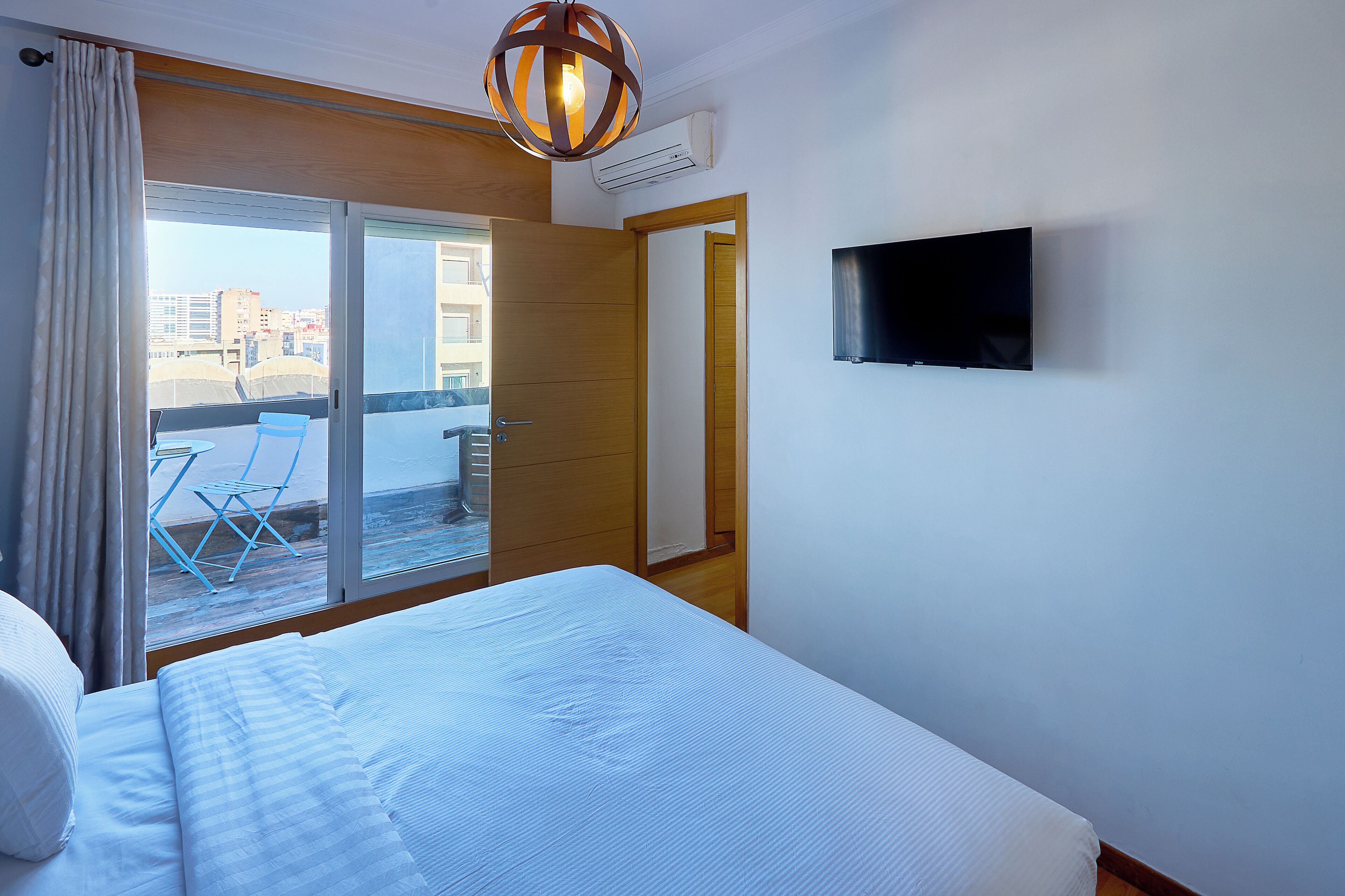 Ett hotellrum med en säng, en TV, en skjutdörr som leder ut till en balkong och utsikt över byggnader.