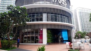 A modern building with a curved facade, large glass windows, and a prominent sign reading 'PARIS BEACH CLUB'. - Resort-Style Pool View Staycation Near NAIA Airport | Affordable & Relaxing (Parañaque)