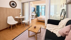 A modern living room with a sofa, chairs, a coffee table, and a bed in the background. - Resort-Style Pool View Staycation Near NAIA Airport | Affordable & Relaxing (Parañaque)