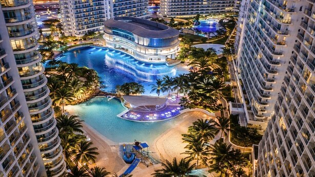 A high-rise hotel with a large swimming pool, palm trees, and a beach area. - Resort-Style Pool View Staycation Near NAIA Airport | Affordable & Relaxing (Parañaque)