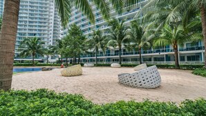 A resort with a pool, palm trees, and modern buildings in the background. - Resort-Style Pool View Staycation Near NAIA Airport | Affordable & Relaxing (Parañaque)
