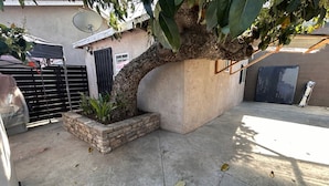 A concrete patio with a tree, a brick planter, a satellite dish, and a garage door. - Lovely 1-bedroom studio with AC in vibrant Los Angeles (Los Angeles)
