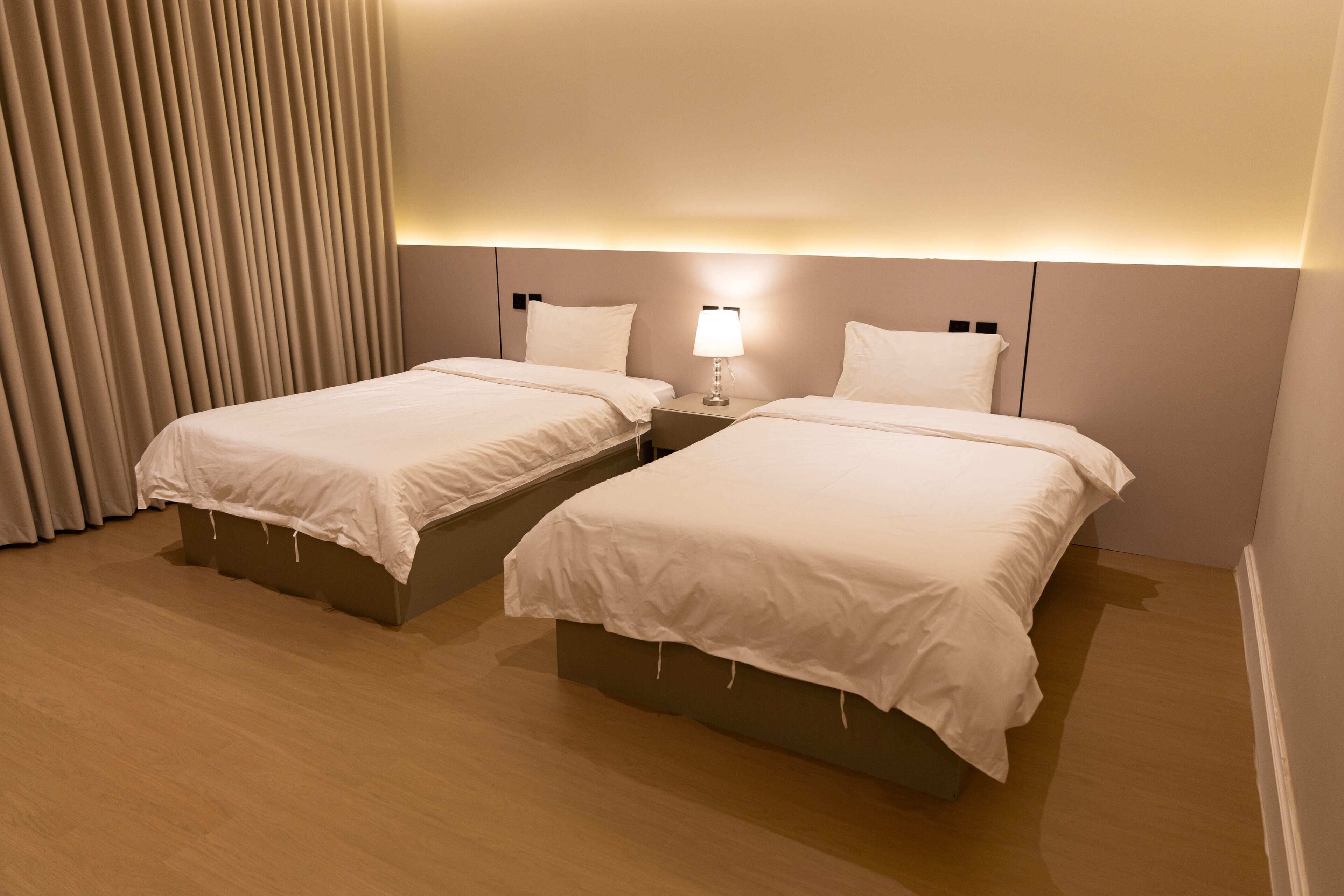 Una habitación de hotel con dos camas, una mesita de noche con lámpara y una cortina.