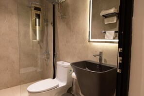 A bathroom with a toilet, shower, sink, and a mirror.