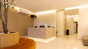 Un espace d’accueil d’hôtel avec un comptoir en marbre, un banc en bois et une plante en pot.