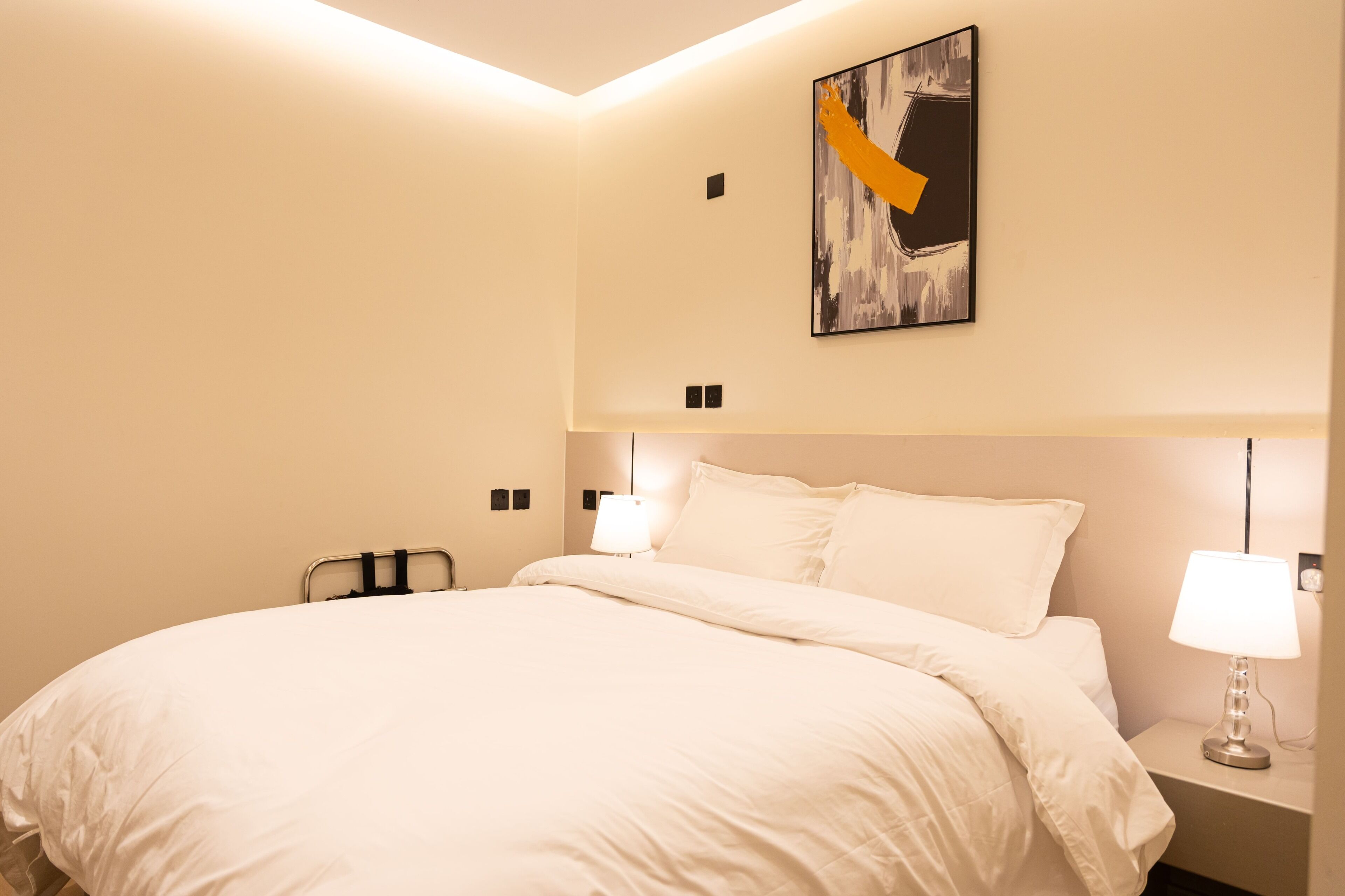 Hotellihuone, jossa on suuri sänky, yöpöytä lampun kanssa, seinälle ripustettu taideteos ja kattovalaisin.