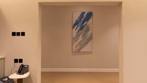 Une pièce avec un tableau accroché au mur, un téléphone posé sur une petite table et un bouton-poussoir sur le mur.