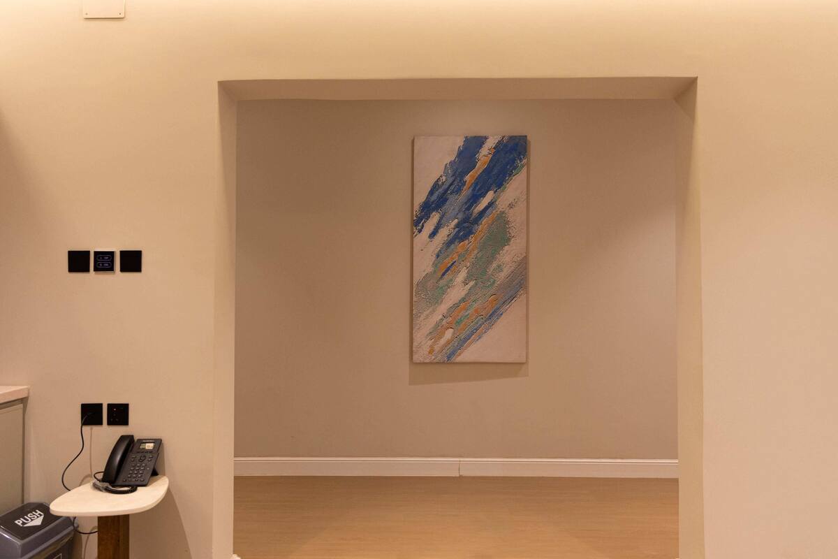 A room with a painting on the wall, a phone on a small table, and a push button on the wall.