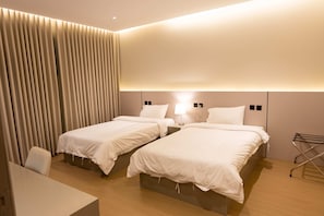 Hotellihuone, jossa on kaksi sänkyä, työpöytä ja tuoli.