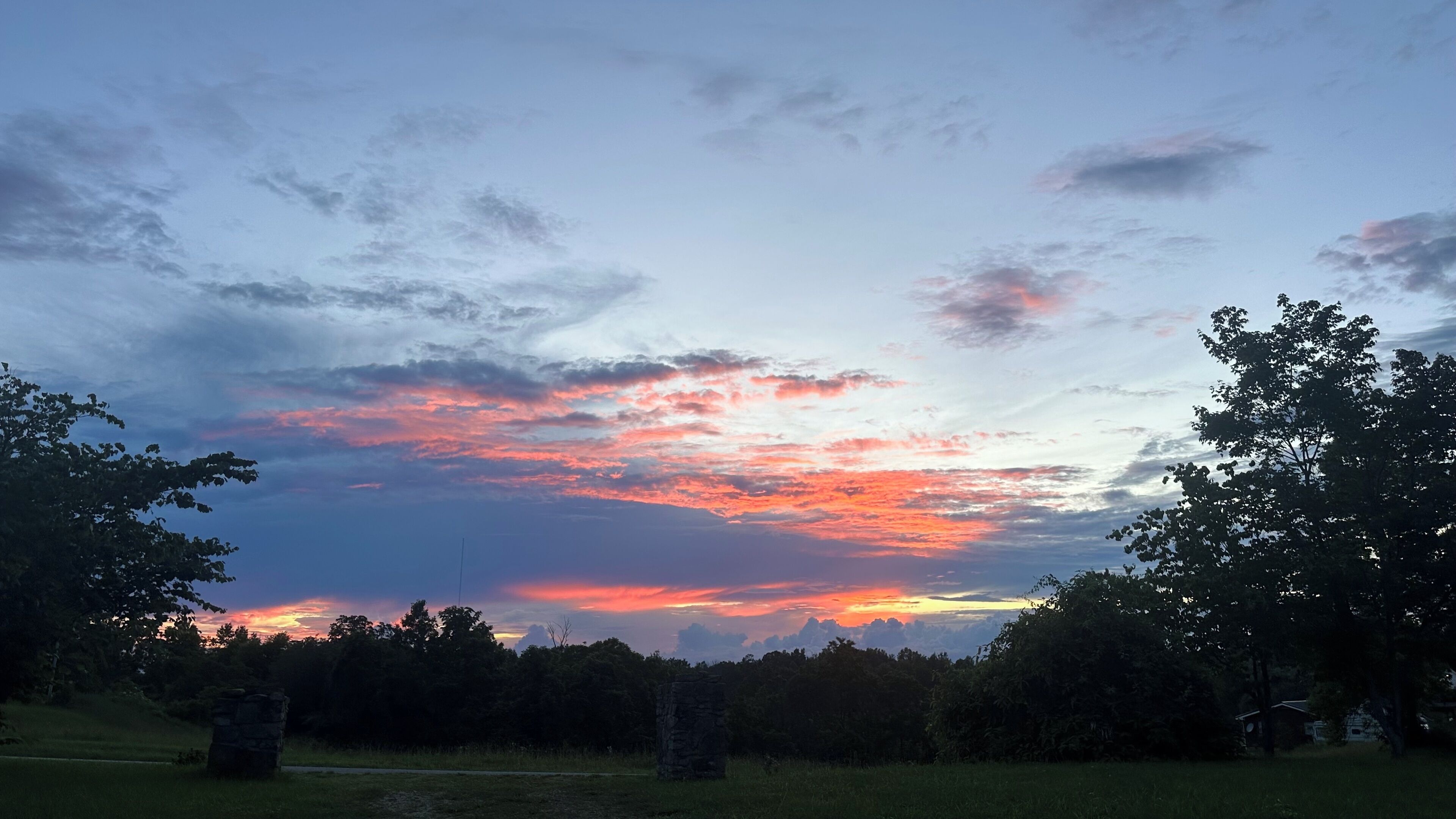 A sunset over a grassy field with trees and a stone structure.