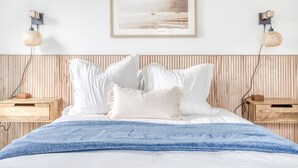 Uma cama com roupa de cama branca, um cobertor azul e um quadro na parede.