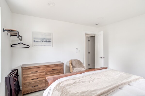 A bedroom with a bed, wooden dresser, radiator, and a door leading to another room.