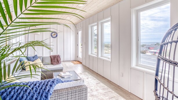 A room with a wooden ceiling, large windows, a wicker sofa, a coffee table, and a potted plant.