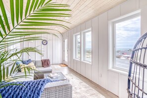 Une pièce avec un plafond en bois, de grandes fenêtres, un canapé en osier, une table basse et une plante en pot.