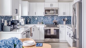 A modern kitchen with white cabinets, a microwave, an oven, and a refrigerator.