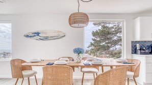 A dining area with a wooden table, wicker chairs, a hanging light fixture, and a wall-mounted artwork.
